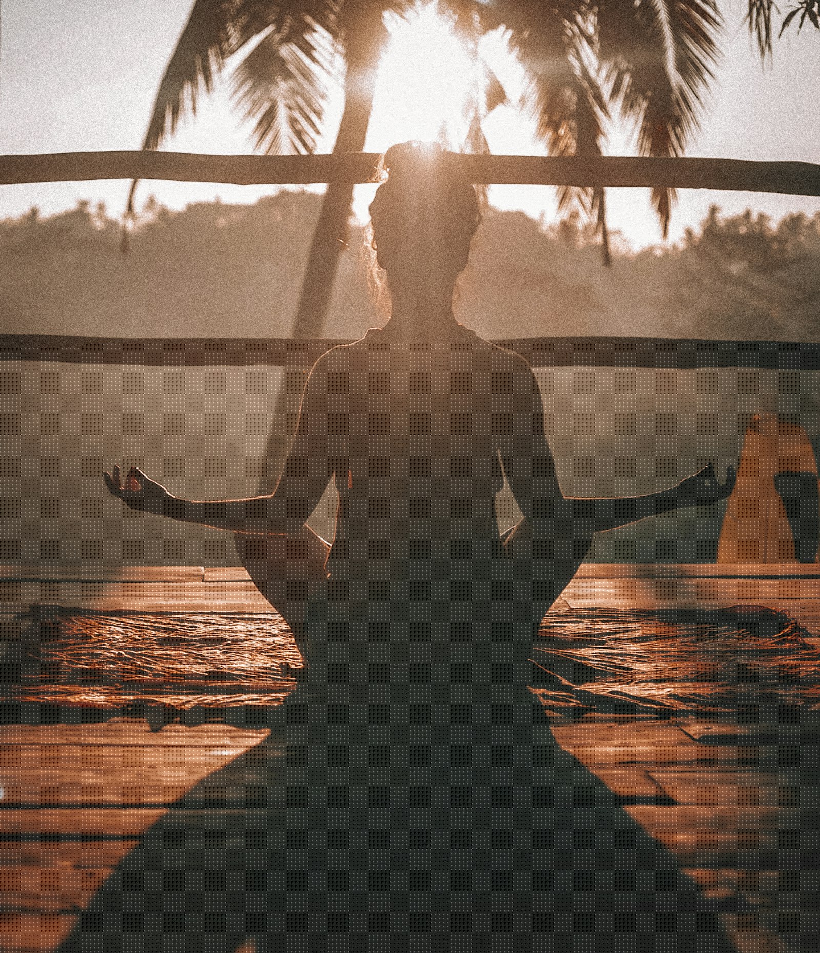 A woman meditating cross-legged at golden sunrise