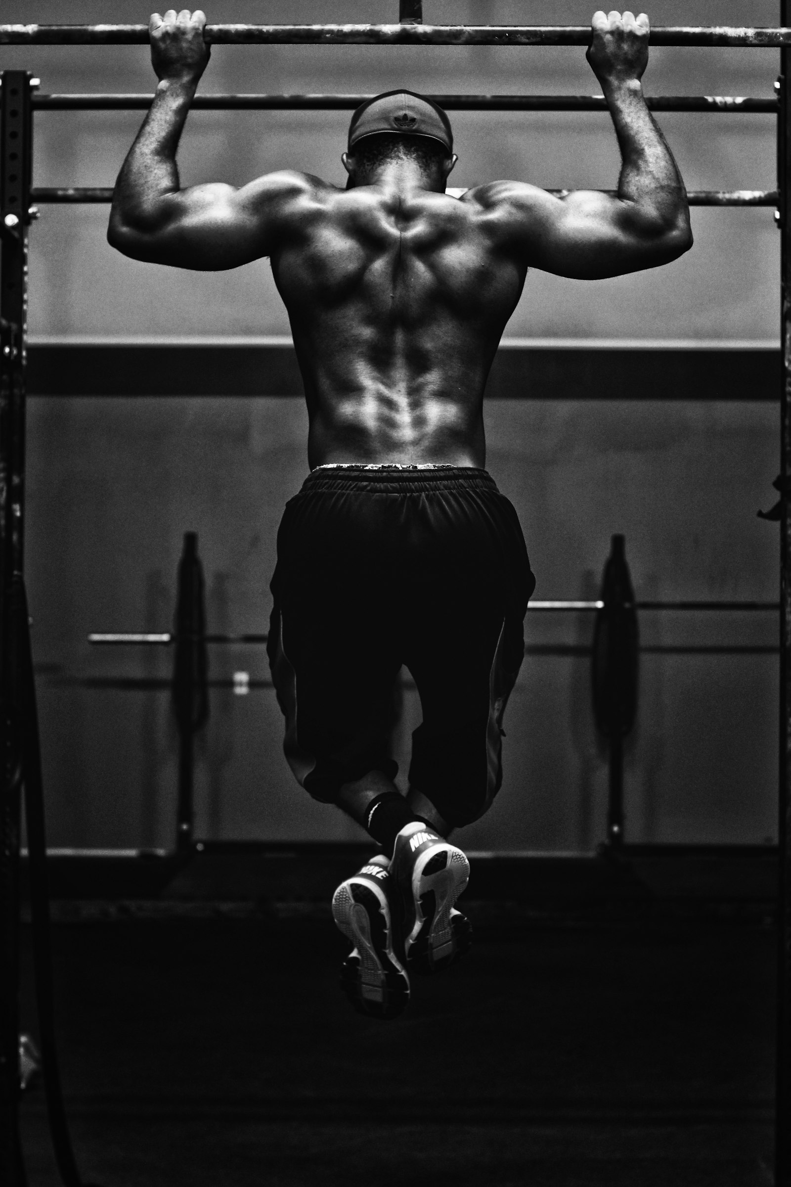 An athlete pulling himself over a bar, mid pull-up, in a dark gym
